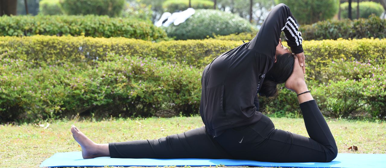 A woman holding a deep seated yoga stretch on a mat in the garden