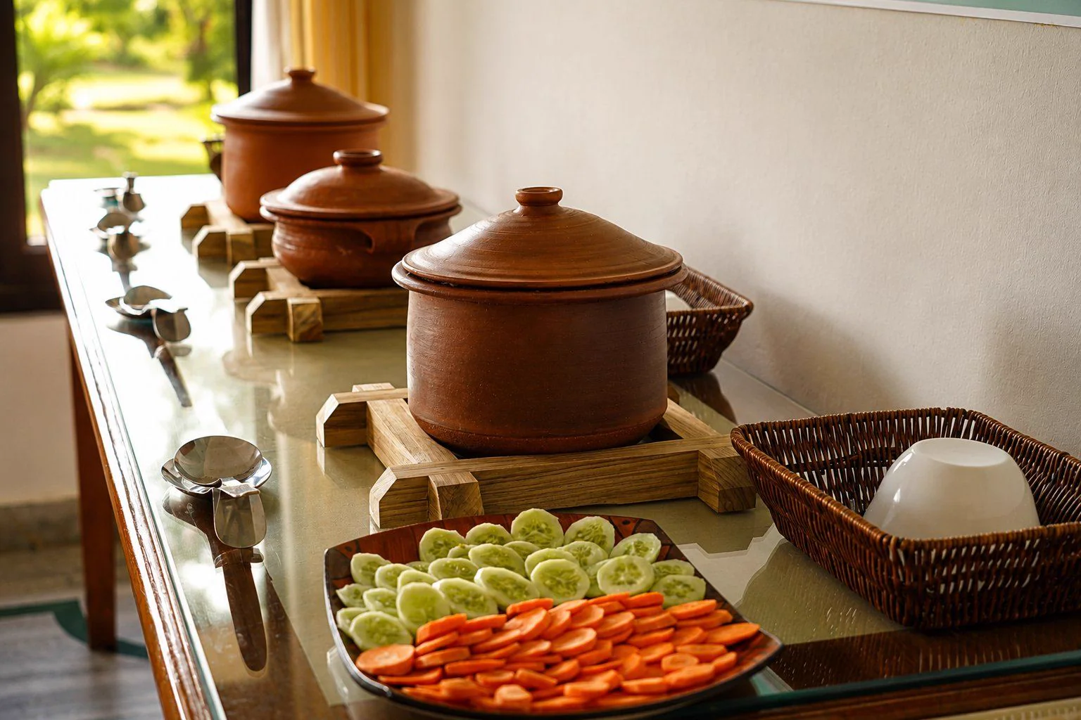 Clay cooking pots and a plate of fresh cucumber and carrot on the serving table in the dining area