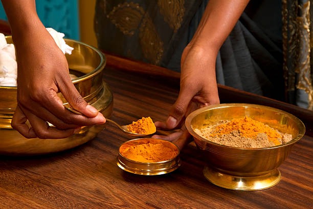 Turmeric and herbal powders being measured into brass bowls for an Ayurveda preparation
